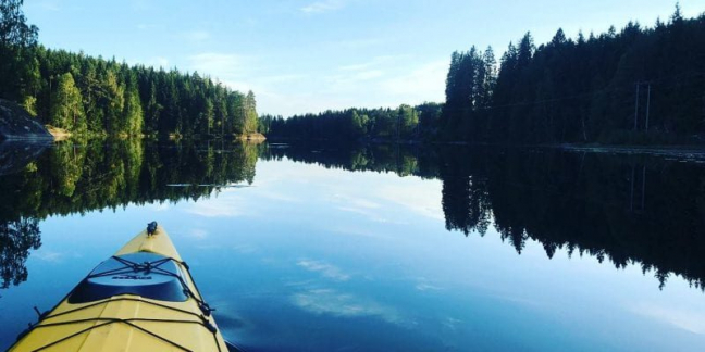 Utsikt over en innsjø omkranset av skog, med fotografen sittende i en kajakk