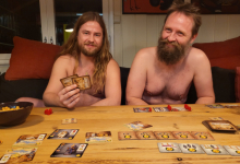 To naturister spiller brettspill, sittende i en sofa hjemme hos noen
